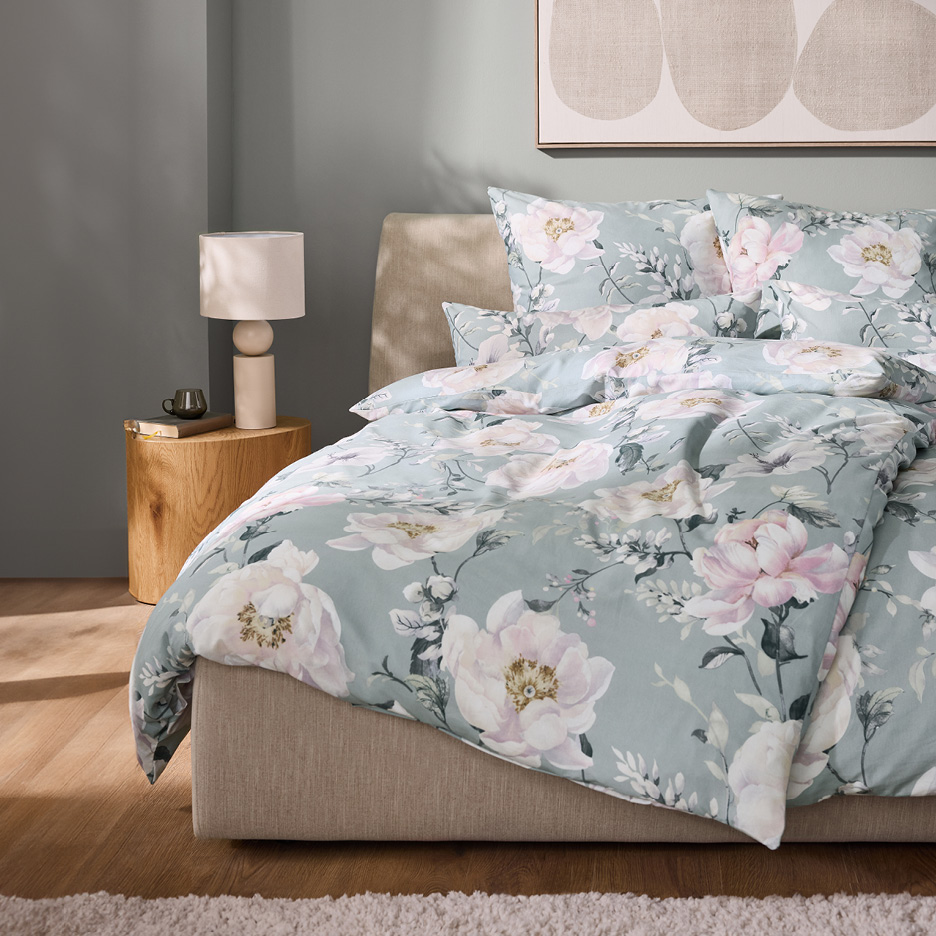 Bedroom with a bed featuring light green floral duvet cover and pillows, and a bedside table.