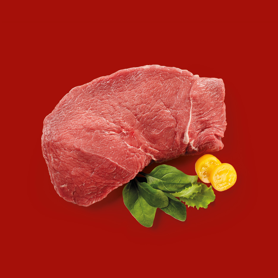 Raw beef steak with spinach leaves and yellow cherry tomato halves on a red background.