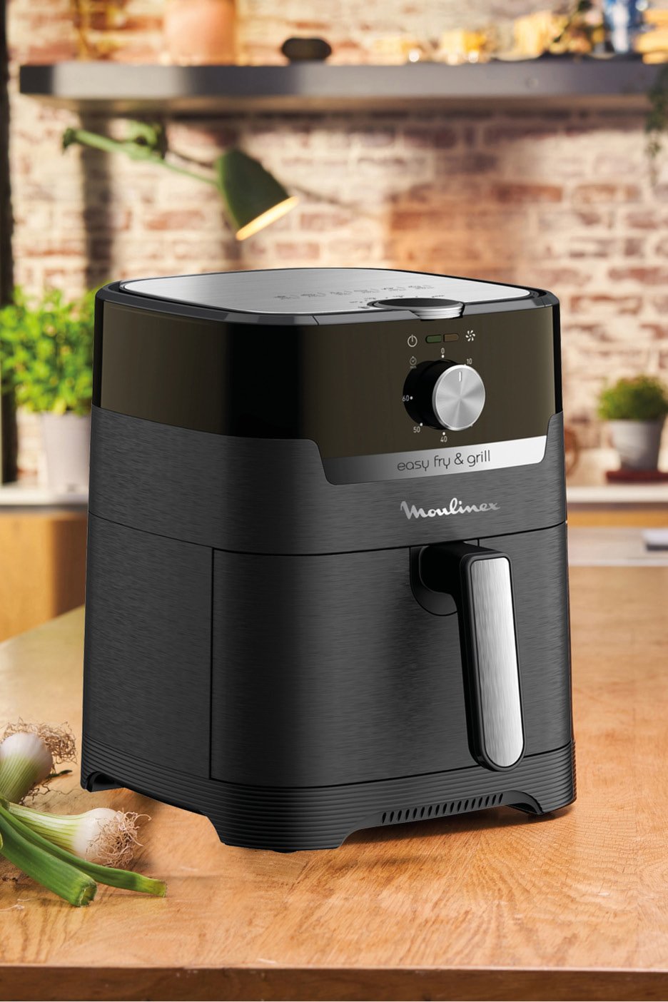 Black air fryer and grill on a wooden counter with spring onions