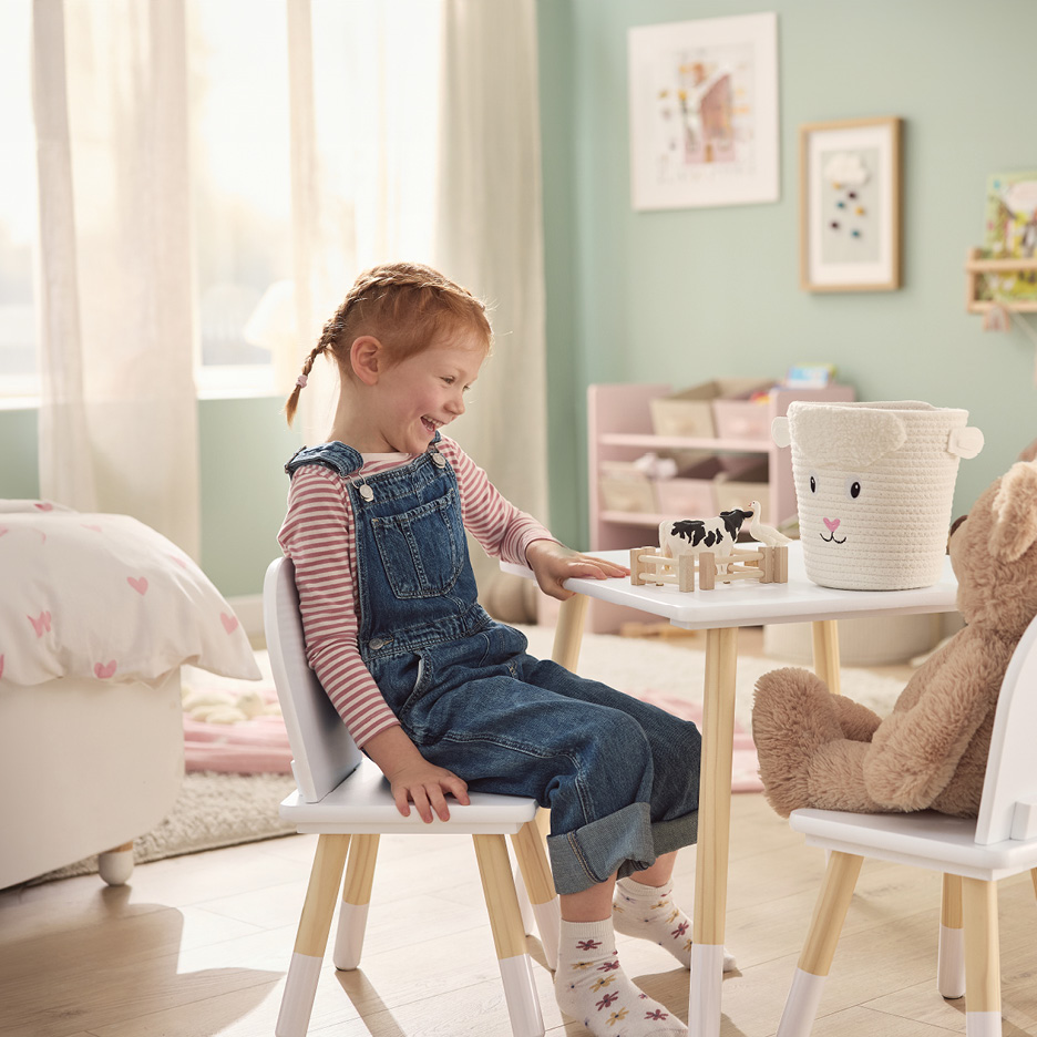 A happy child playing with a toy farm set and a sheep-themed storage basket on a white table.