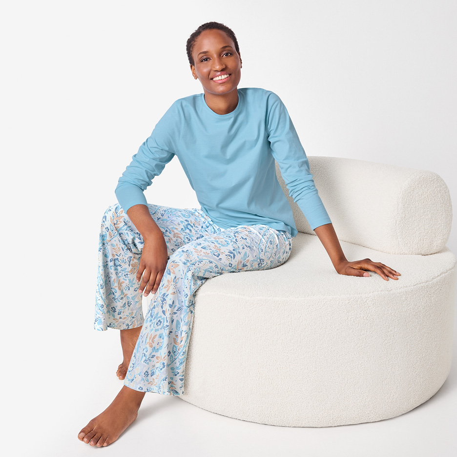 Woman in blue long-sleeve top and floral print pyjama bottoms, sitting on a white chair.