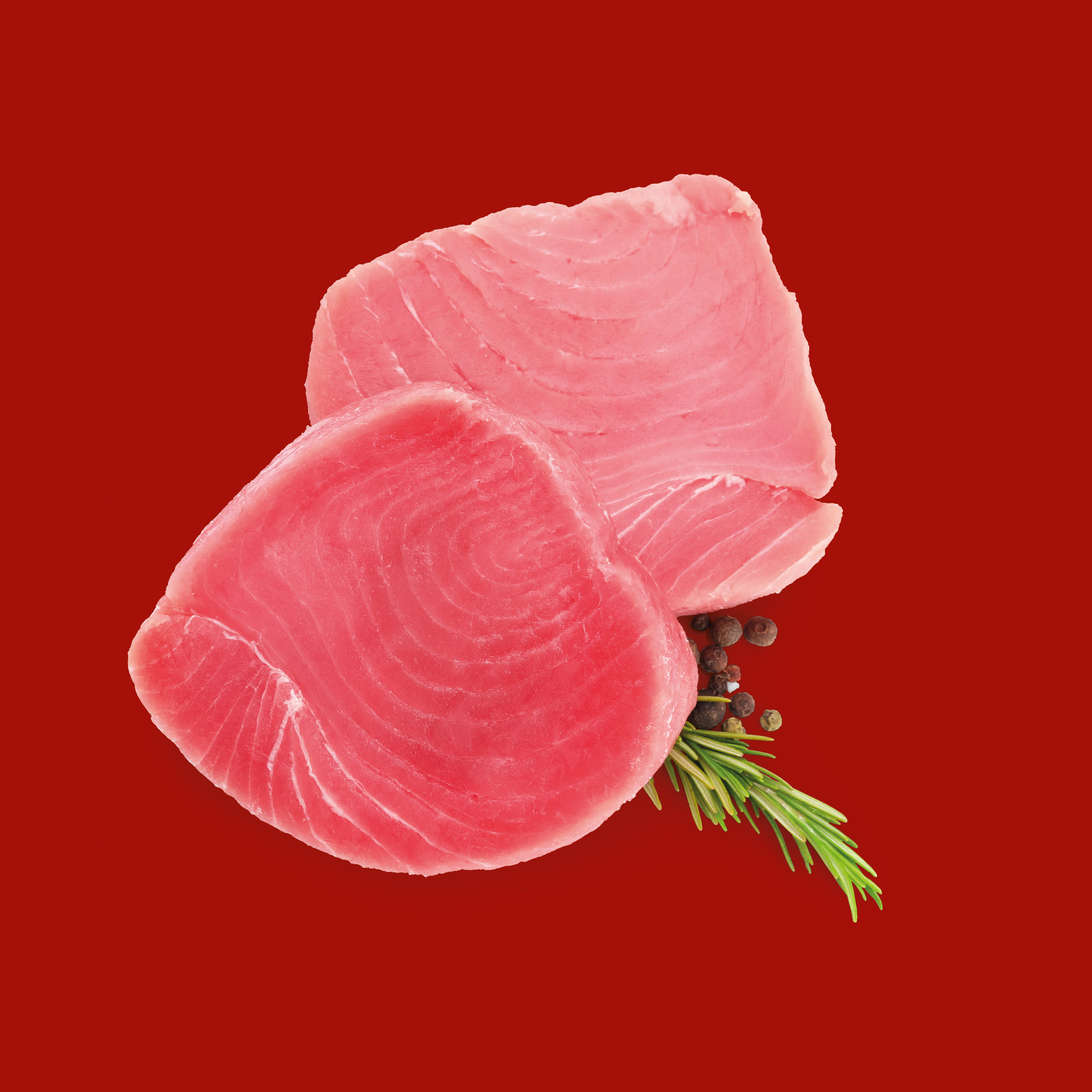 Two raw tuna steaks with rosemary and peppercorns on a red background.