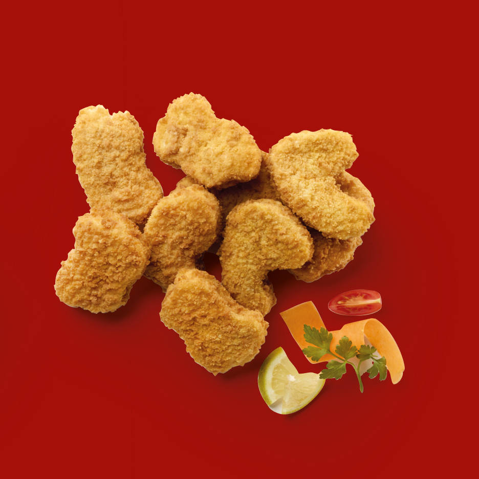 Crispy chicken nuggets with a lemon wedge, tomato slice, carrot curl, and parsley on red.