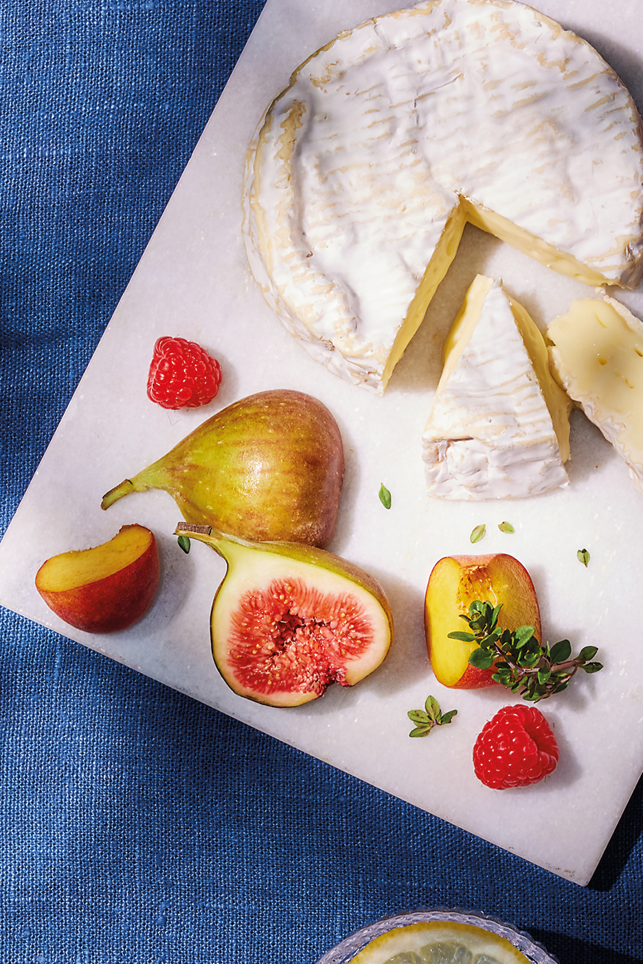 Brie cheese with figs, raspberries, and peaches on a marble board.