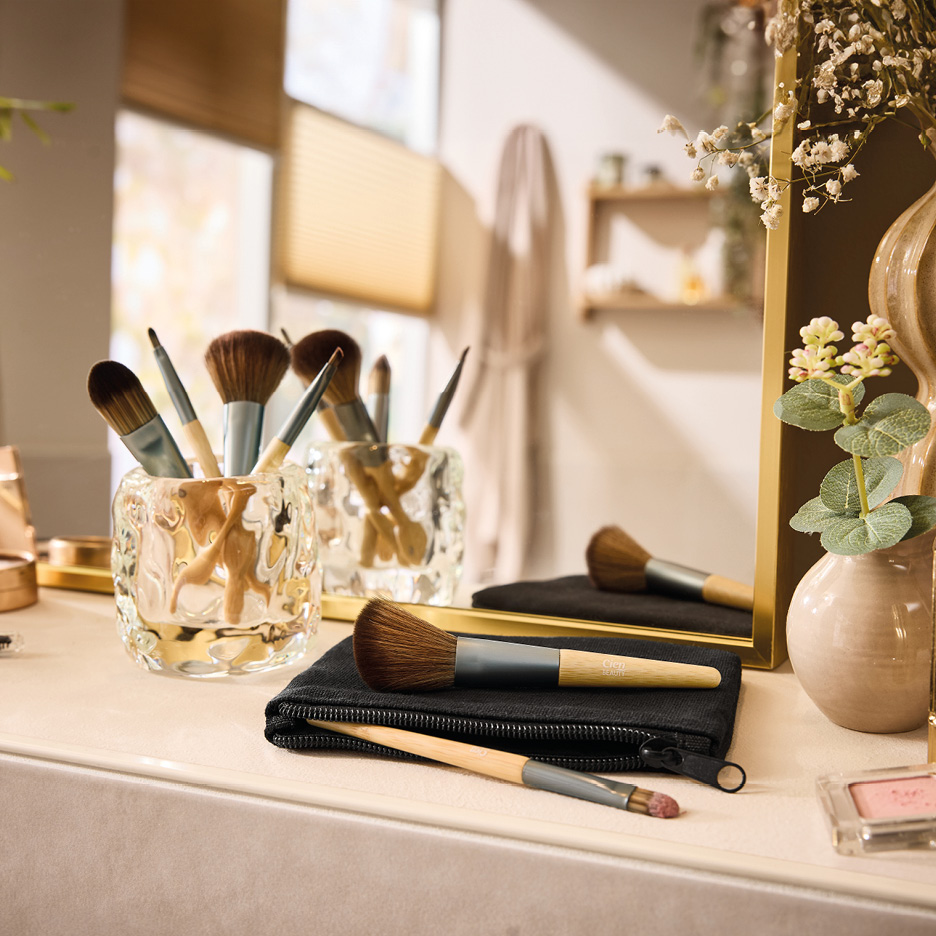 Makeup brushes in glass holders and on a black pouch, with a mirror and decor.