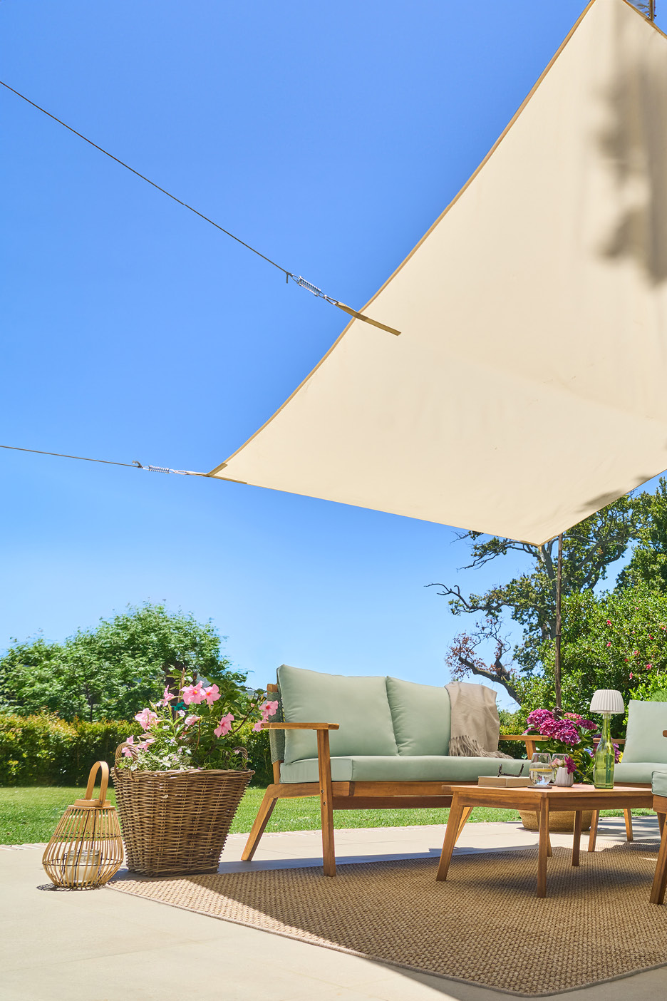Outdoor patio with wooden garden furniture, light green cushions, and a beige sun shade.