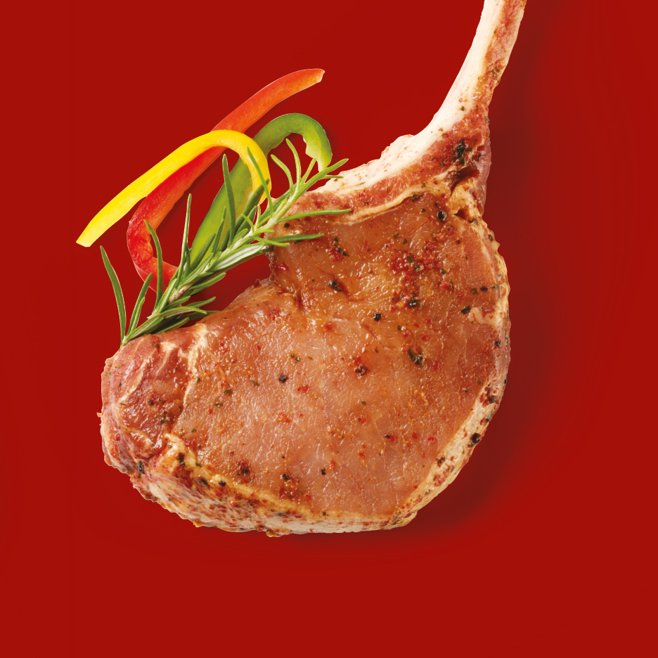 Seasoned pork chop with bone, garnished with rosemary and bell pepper strips on a red background.