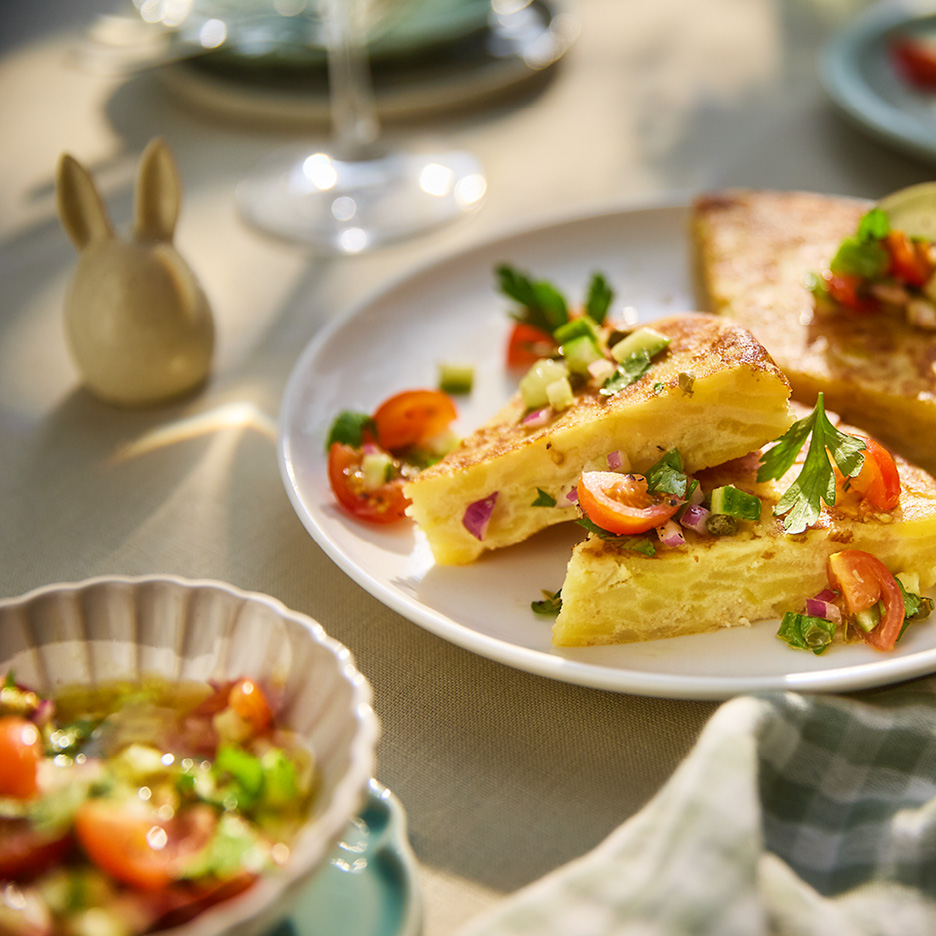 Slices of potato omelette topped with fresh tomato and herb salsa, served on a white plate.