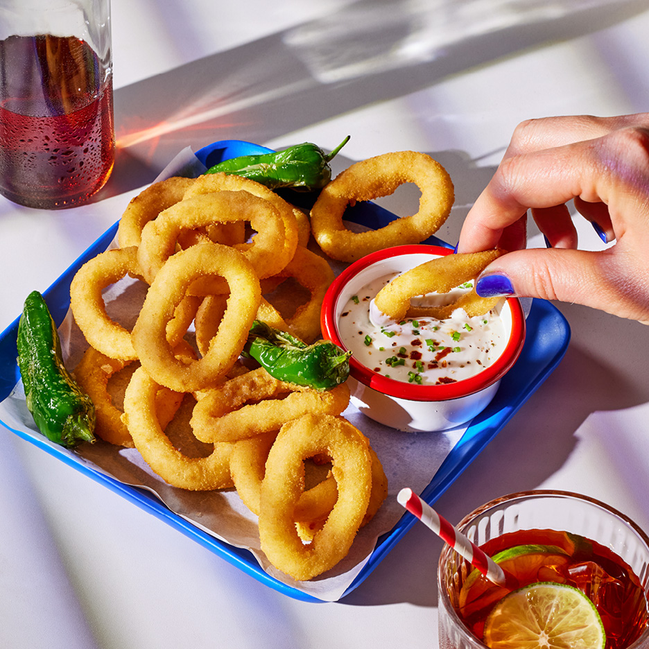 Crispy onion rings with green peppers and dipping sauce, next to a refreshing drink.