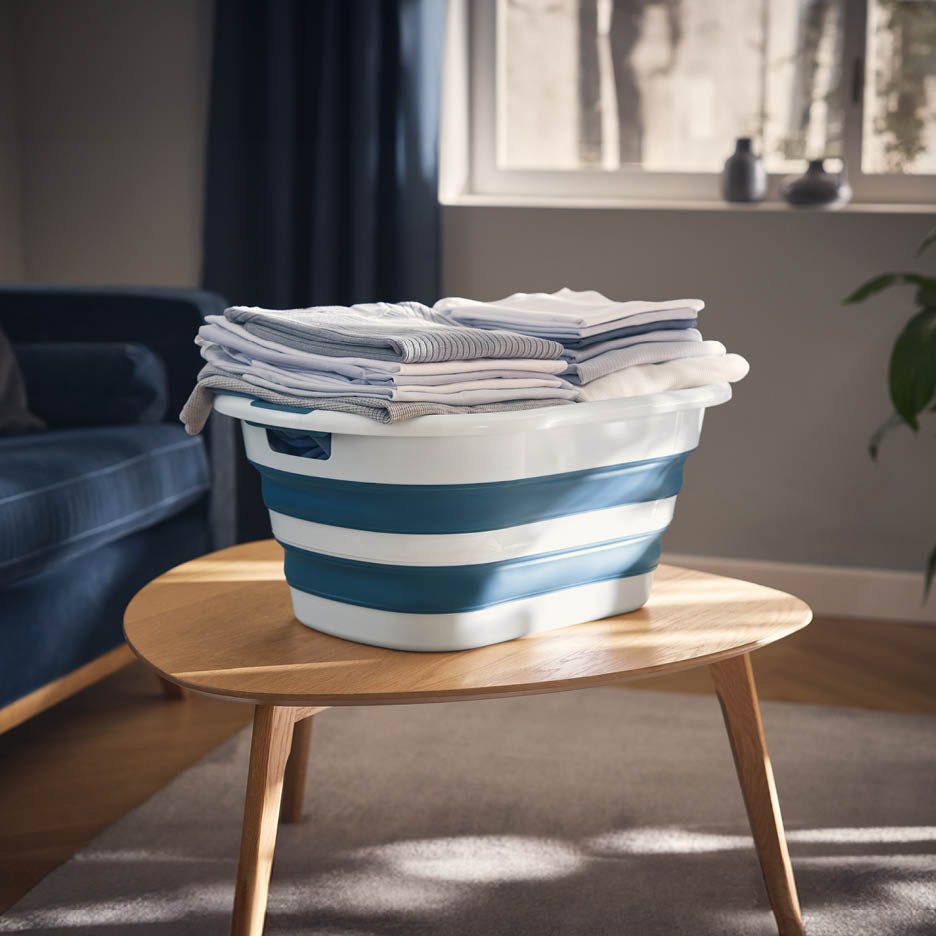 Foldable laundry basket with clean, folded clothes on a wooden coffee table.