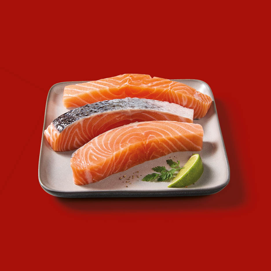 Three fresh salmon fillets on a grey plate, garnished with a lime wedge and parsley.