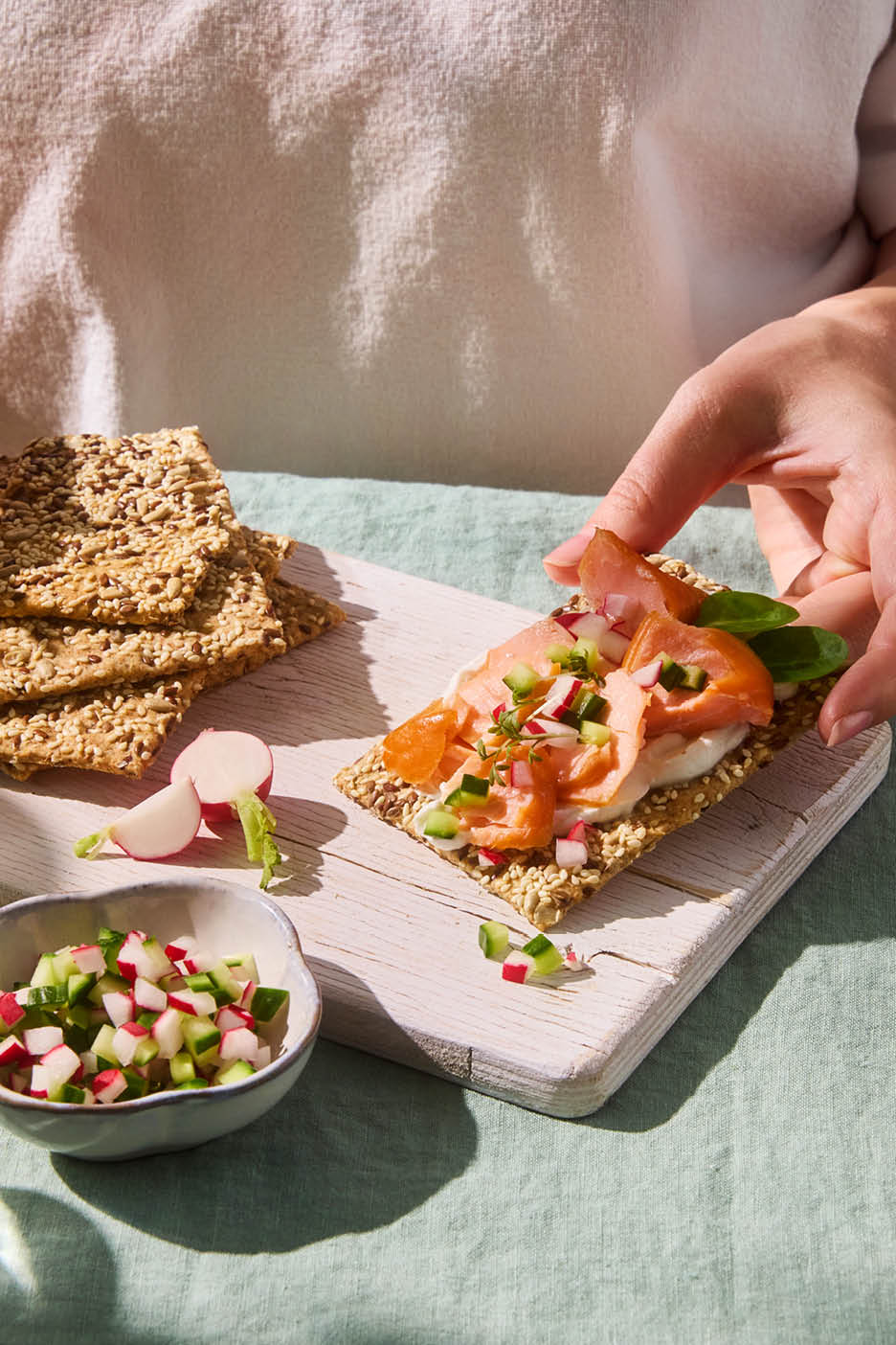 Hand holding a crispbread with smoked salmon, cream cheese, and diced vegetables.