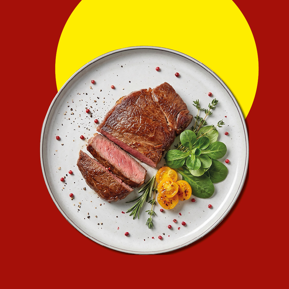 Cooked steak, sliced, with fresh greens, cherry tomatoes, and spices on a white plate.