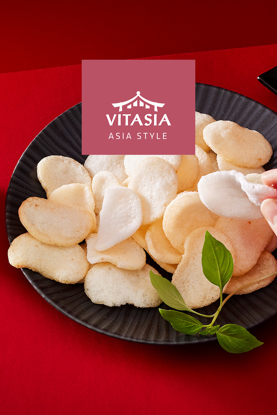 A plate of Asian-style prawn crackers with a hand picking one up, on a red background.