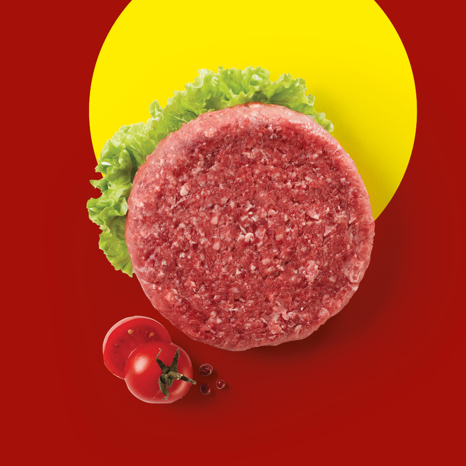 Raw beef burger patty with lettuce, tomato, and peppercorns on a red and yellow background.