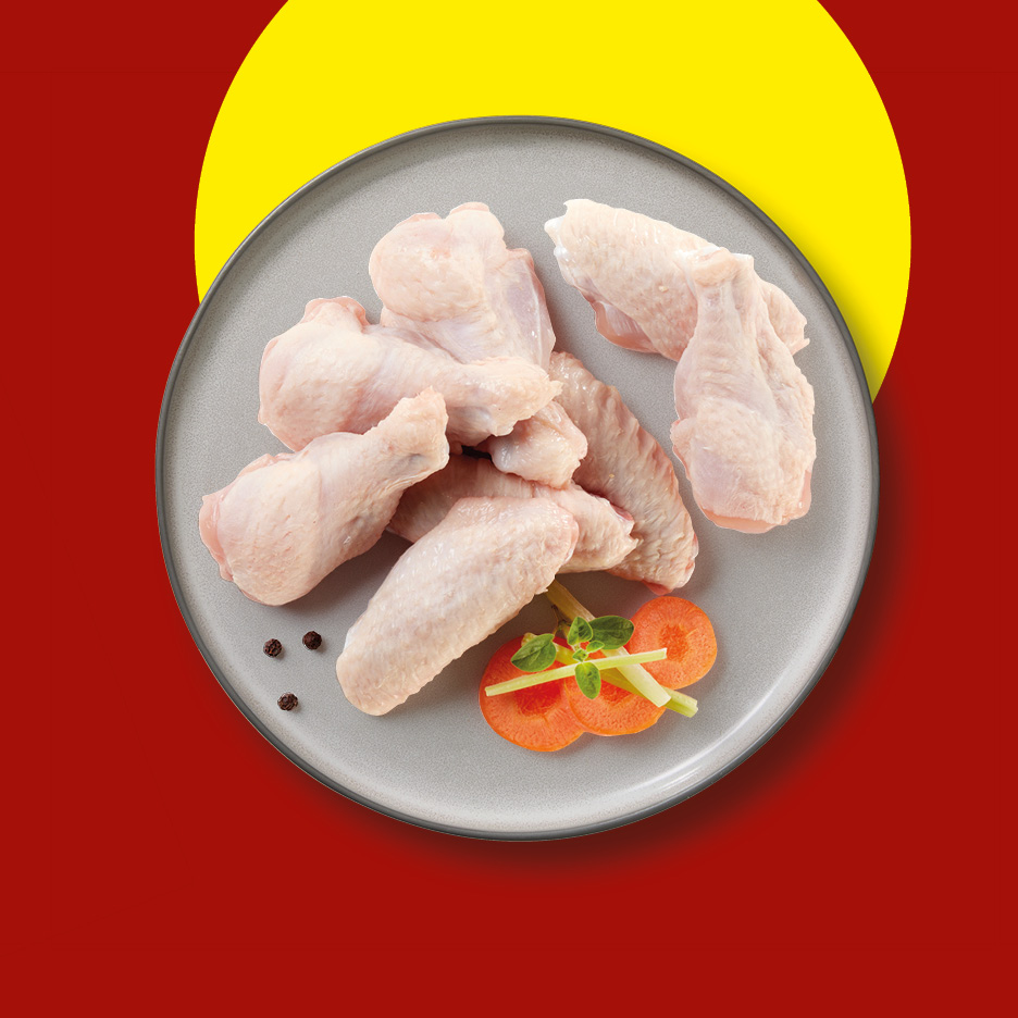 Raw chicken wings and drumettes on a grey plate with carrot slices and herbs.