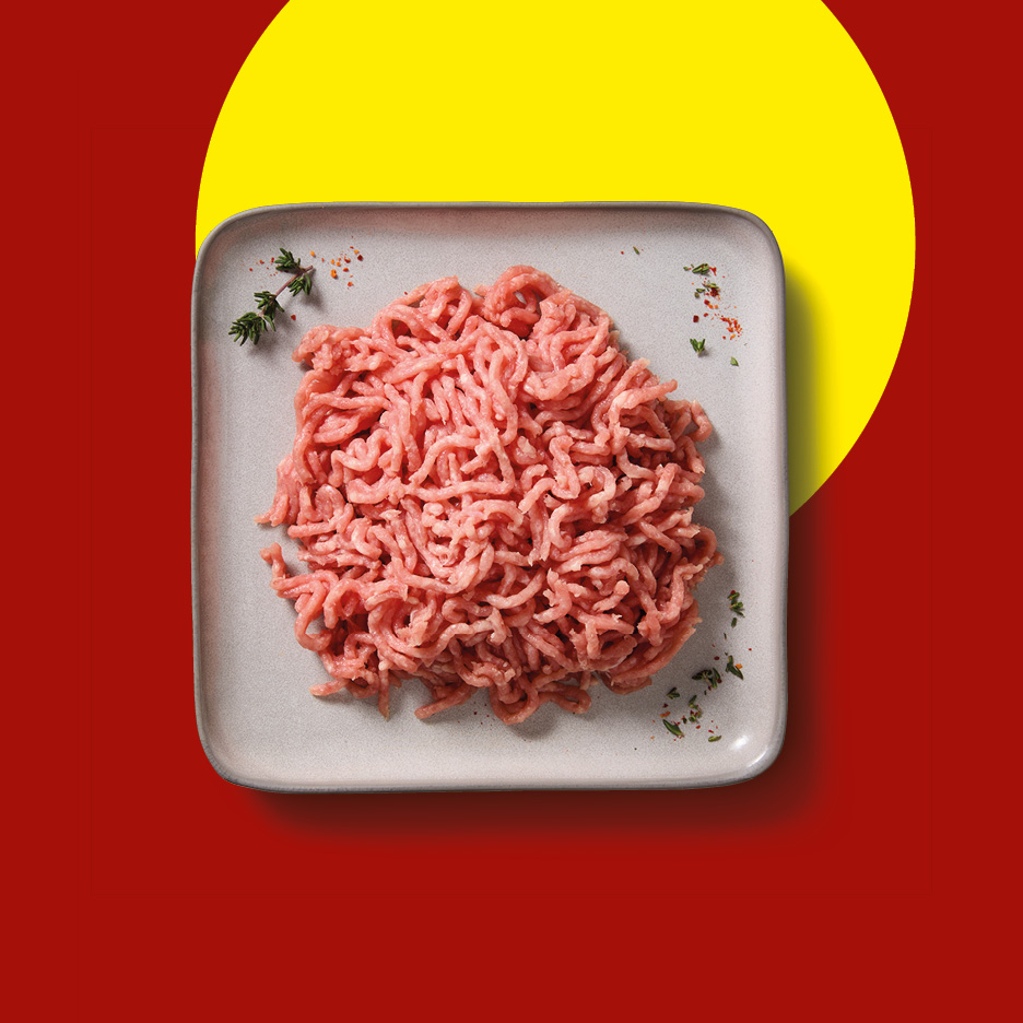 Raw minced meat on a grey plate, garnished with herbs, on a red and yellow background.
