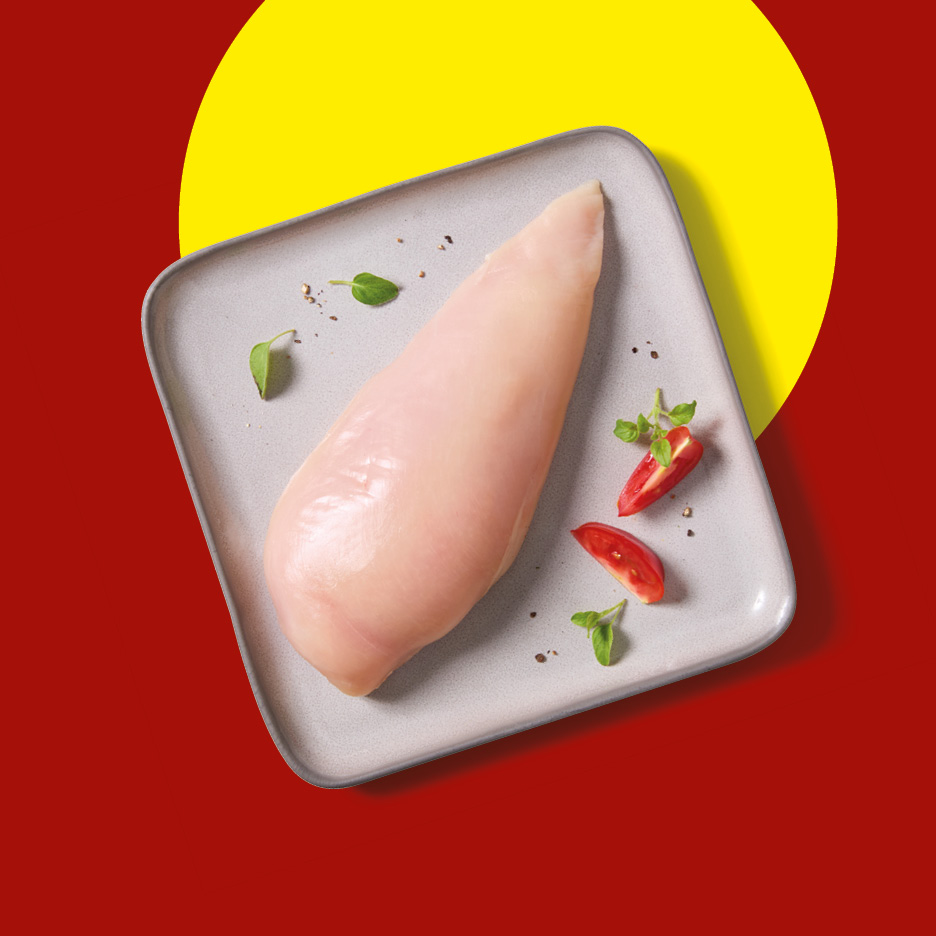 Raw chicken breast on a grey plate with tomato wedges and herbs.