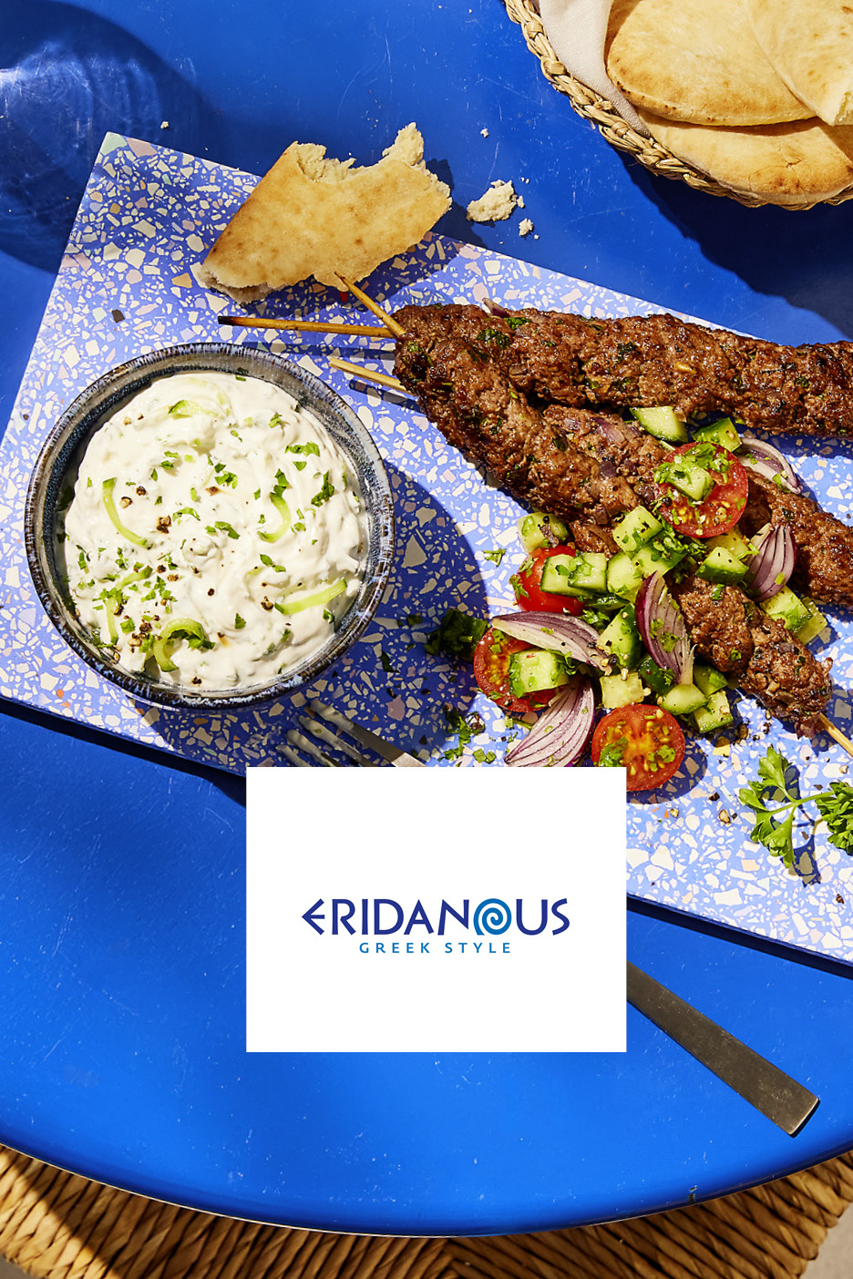 Greek-style kebabs with tzatziki, salad, and pita bread on a blue table.