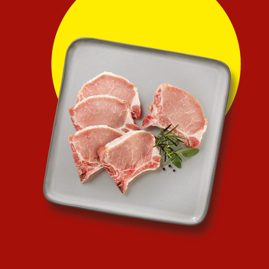 Raw pork chops with herbs and peppercorns on a grey plate, against a red and yellow background.