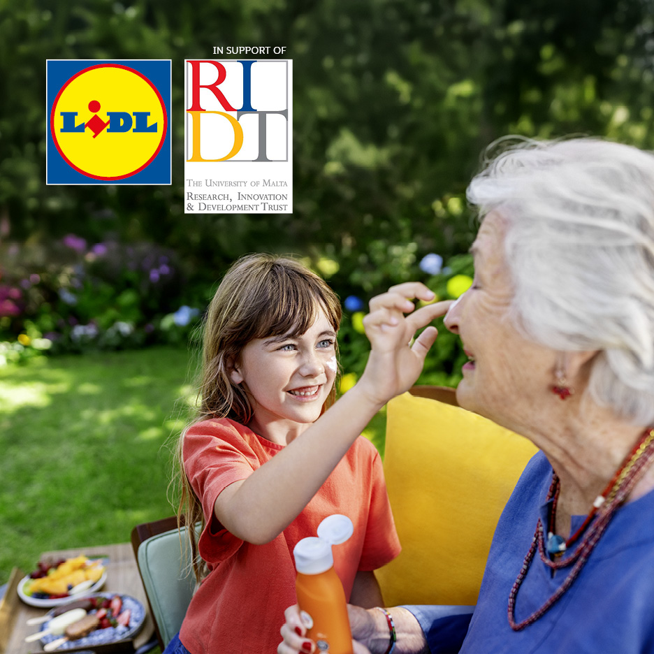 A child applies sunscreen to an elderly woman's nose in a garden, with a bottle of sunscreen and snacks nearby. Text: 'IN SUPPORT OF THE UNIVERSITY OF MALTA RESEARCH, INNOVATION & DEVELOPMENT TRUST'