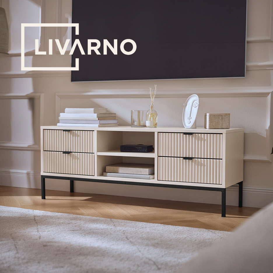 Cream TV stand with fluted drawers, black legs, and a TV above, styled with books and decor.
