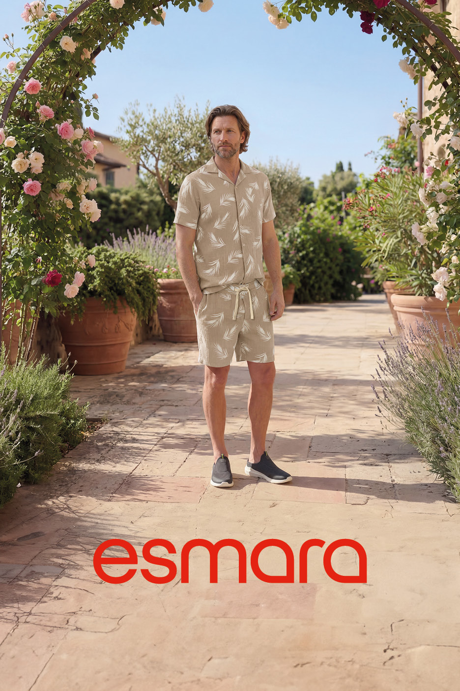 Man in a beige leaf-patterned shirt and shorts, standing under a rose archway.