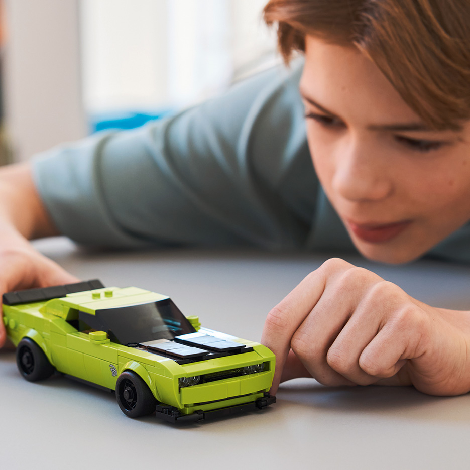 Boy playing with a lime green toy car on a table.