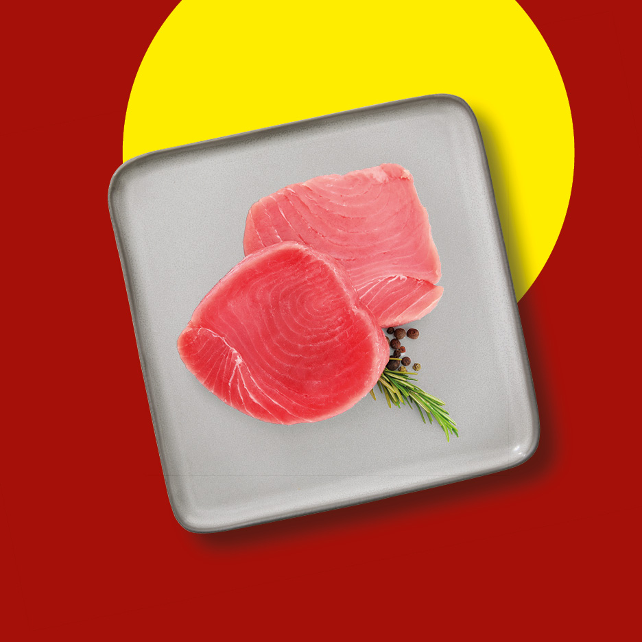 Two fresh tuna steaks with rosemary and peppercorns on a grey tray.
