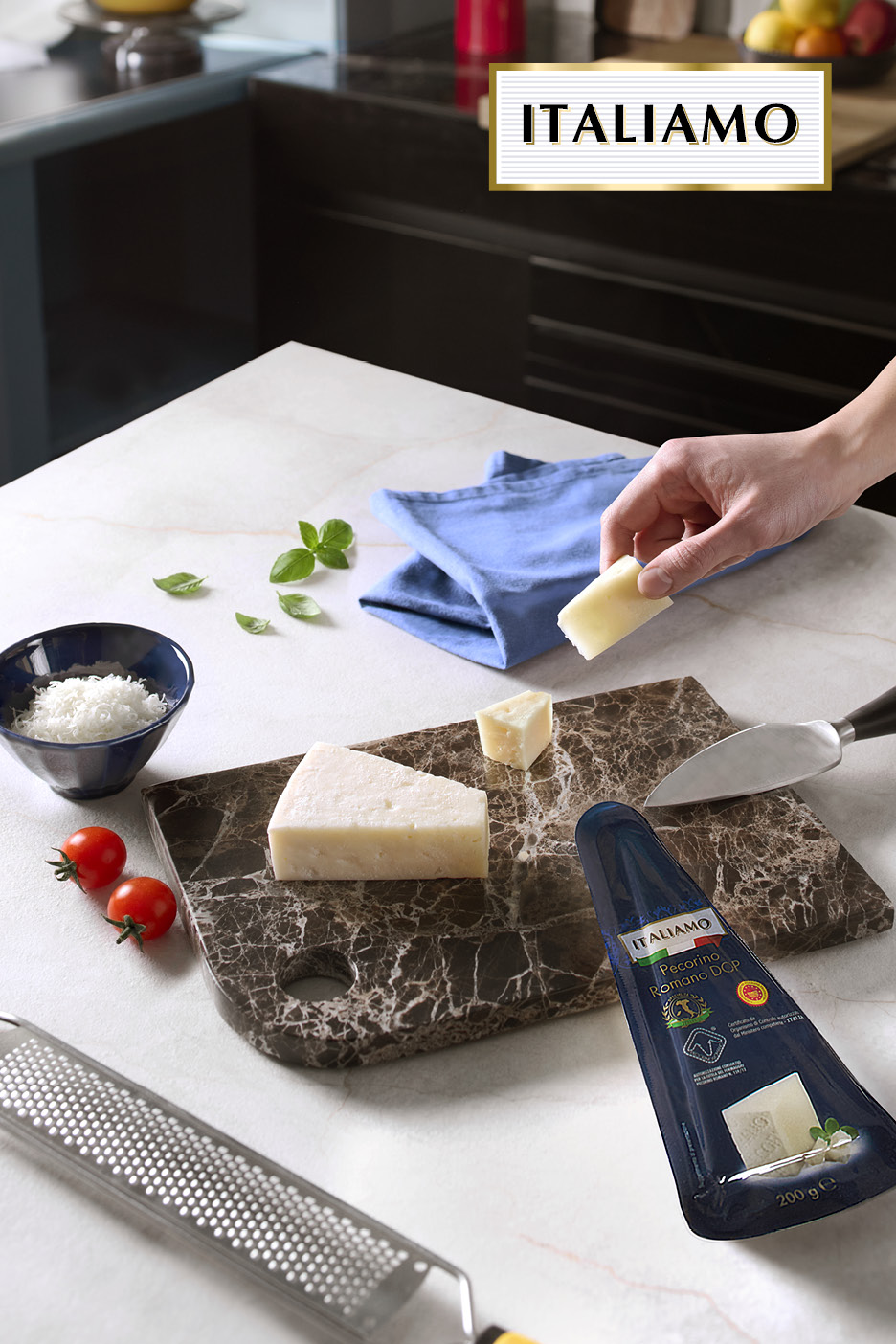 Pecorino Romano cheese on a marble board with a grater, tomatoes, and basil.