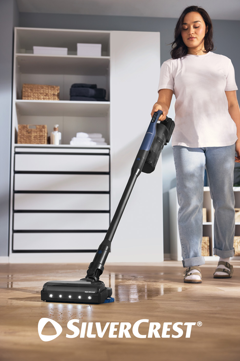 Woman cleaning a wooden floor with a cordless stick vacuum cleaner, with a closet in the background.