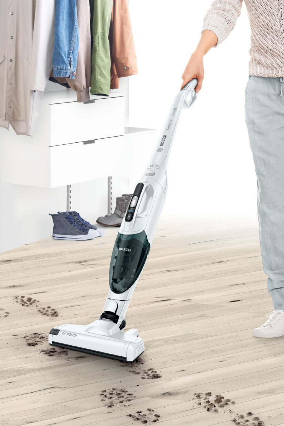 A person vacuuming paw prints off a wooden floor with a white Bosch cordless vacuum.