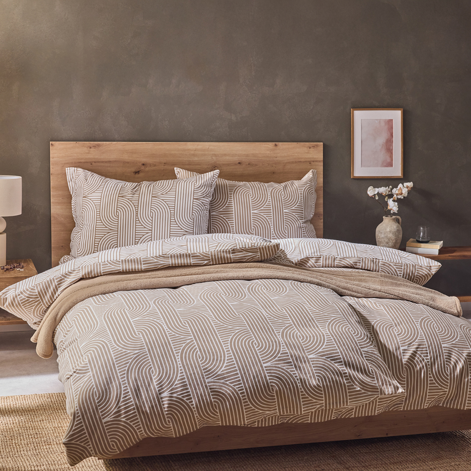 A bed with a wooden headboard and beige bedding featuring a geometric pattern.