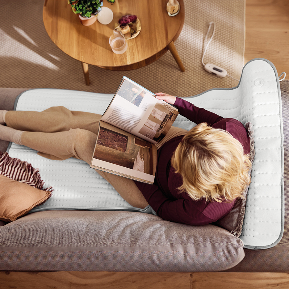 Woman reading a magazine on a heated mattress pad on a sofa.