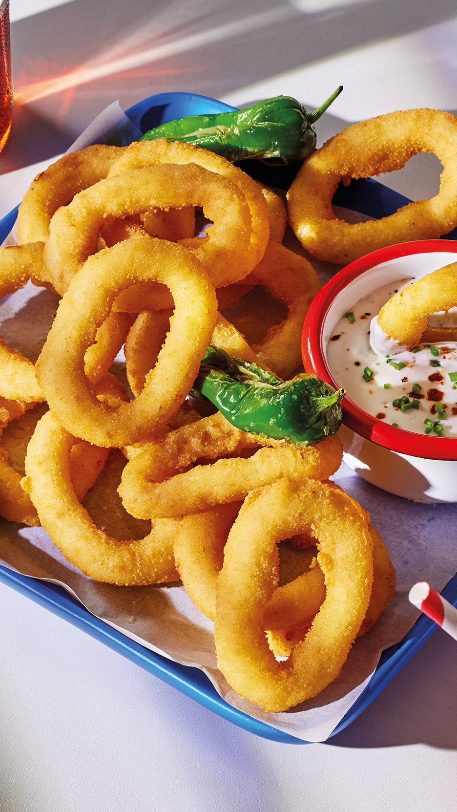 A blue tray filled with golden onion rings, green peppers, and a dipping sauce.