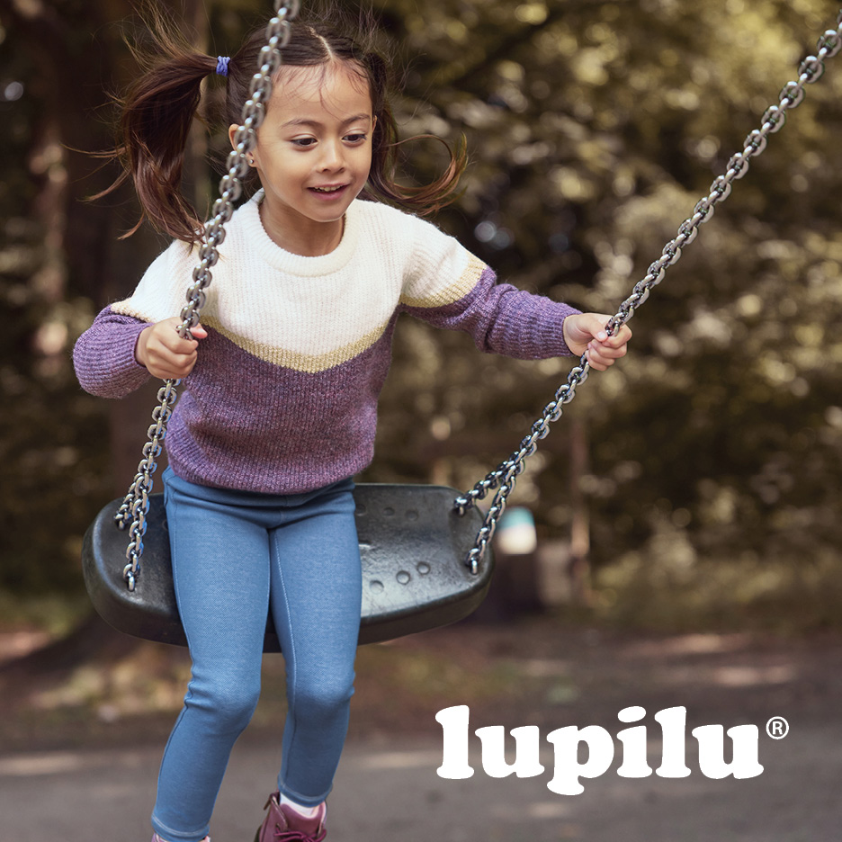 A girl on a swing wearing a purple and white knit sweater and blue leggings.