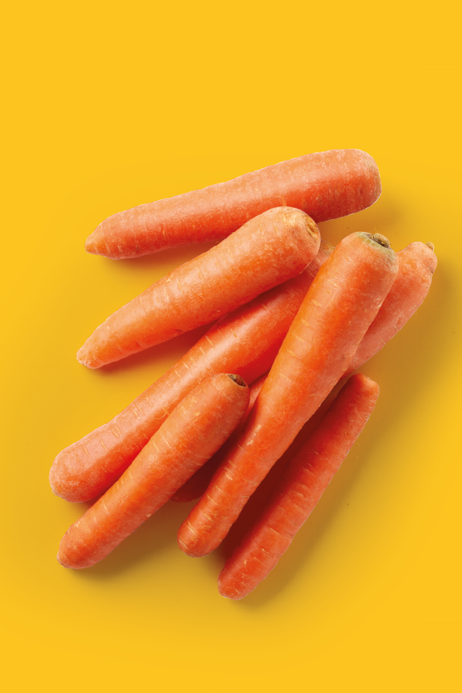 A pile of fresh, orange carrots on a bright yellow background.