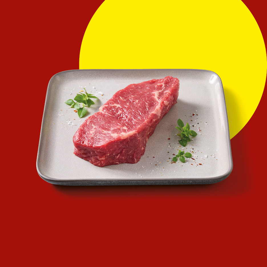 Raw beef steak on a grey plate with herbs and spices, set against a red and yellow background