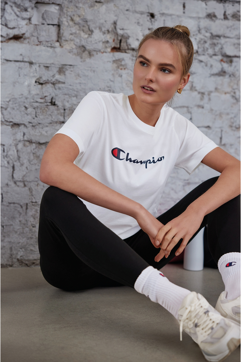 Woman wearing white Champion t-shirt and black leggings, sitting on the floor.