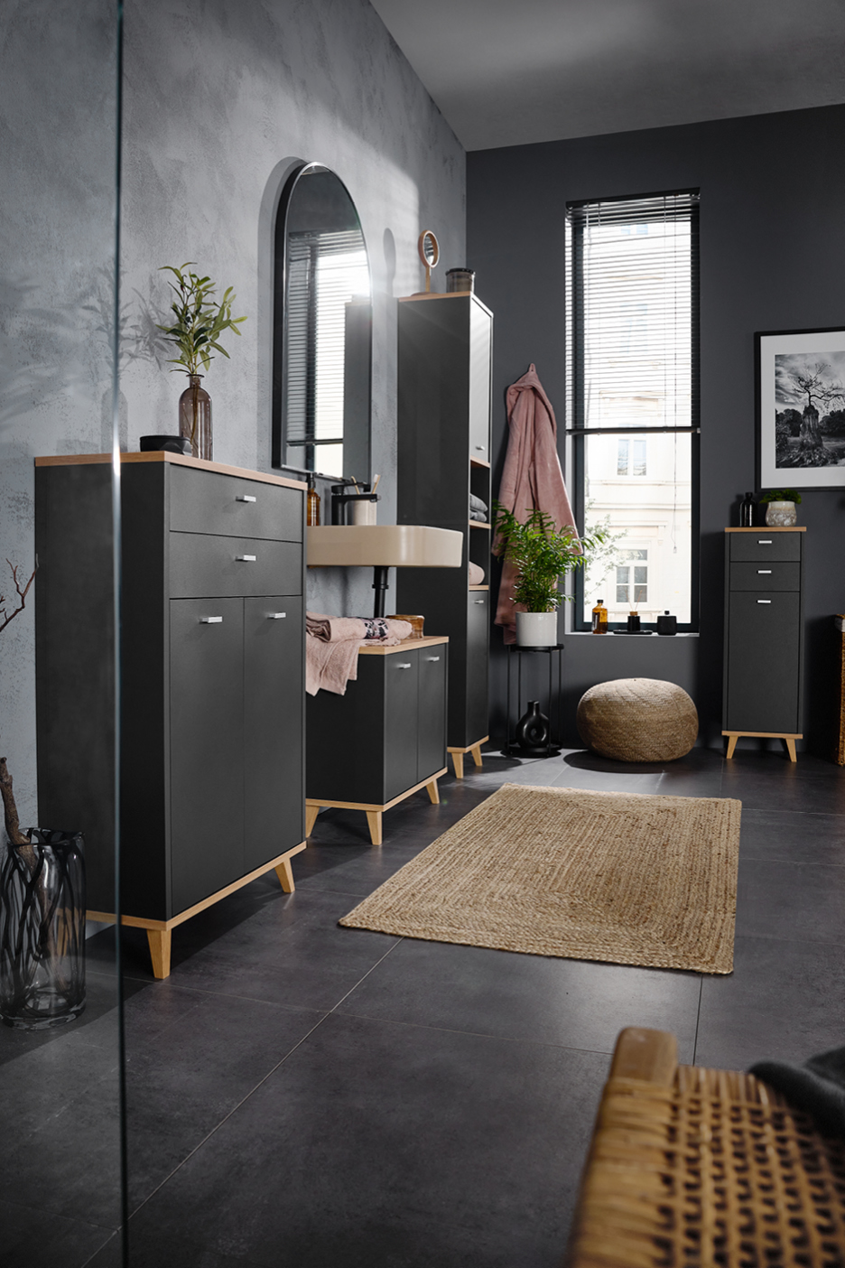 Modern bathroom with dark grey cabinets, wooden accents, and a large arched mirror.