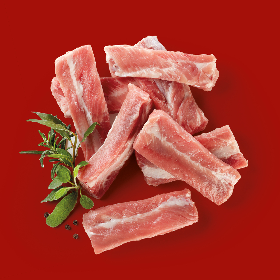 Raw pork ribs with herbs and peppercorns on a red background.