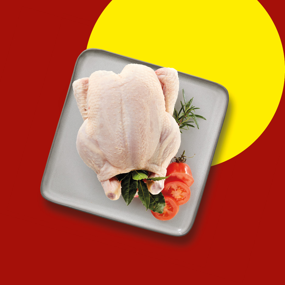 A whole raw chicken on a grey plate with tomatoes and herbs, set against a red and yellow background.