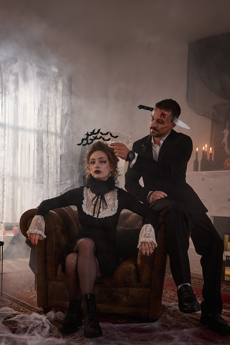 Halloween-themed couple in costumes, with a woman in a black dress and a man with a fake knife in his head.