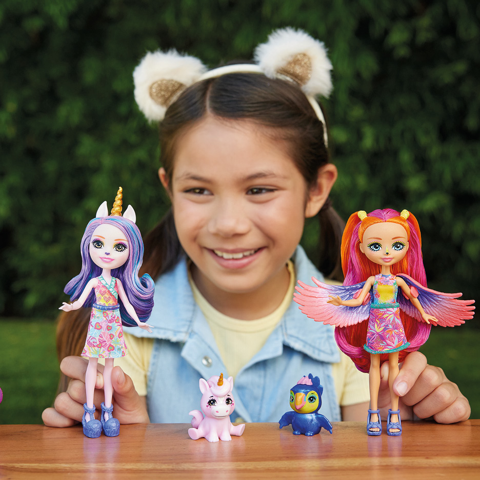 A girl playing with colorful doll figures and small animal toys on a wooden table.