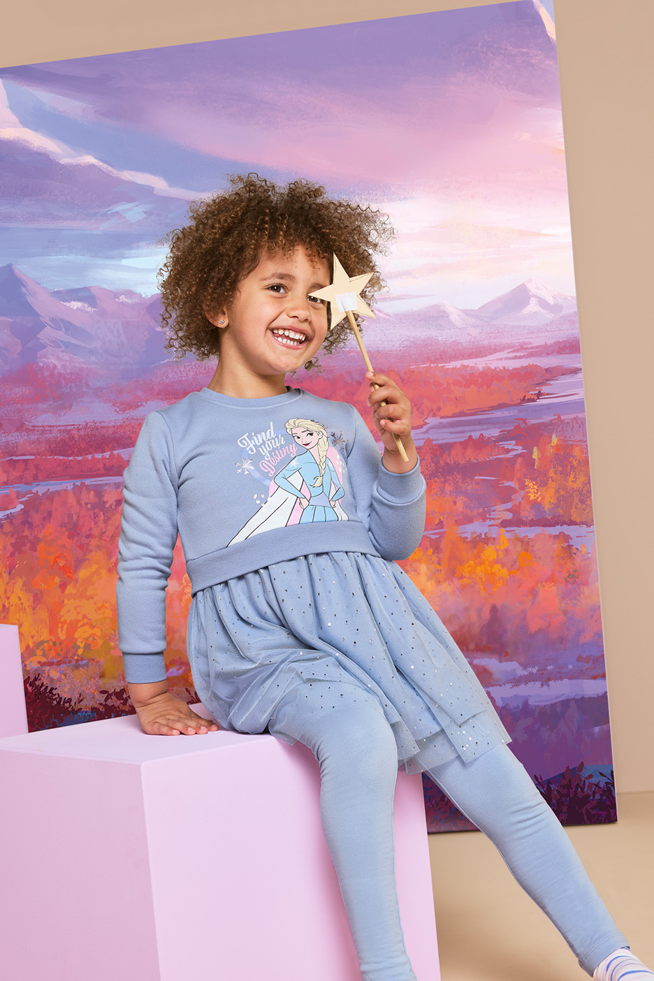 Young girl in a blue Frozen-themed dress and leggings holding a star wand
