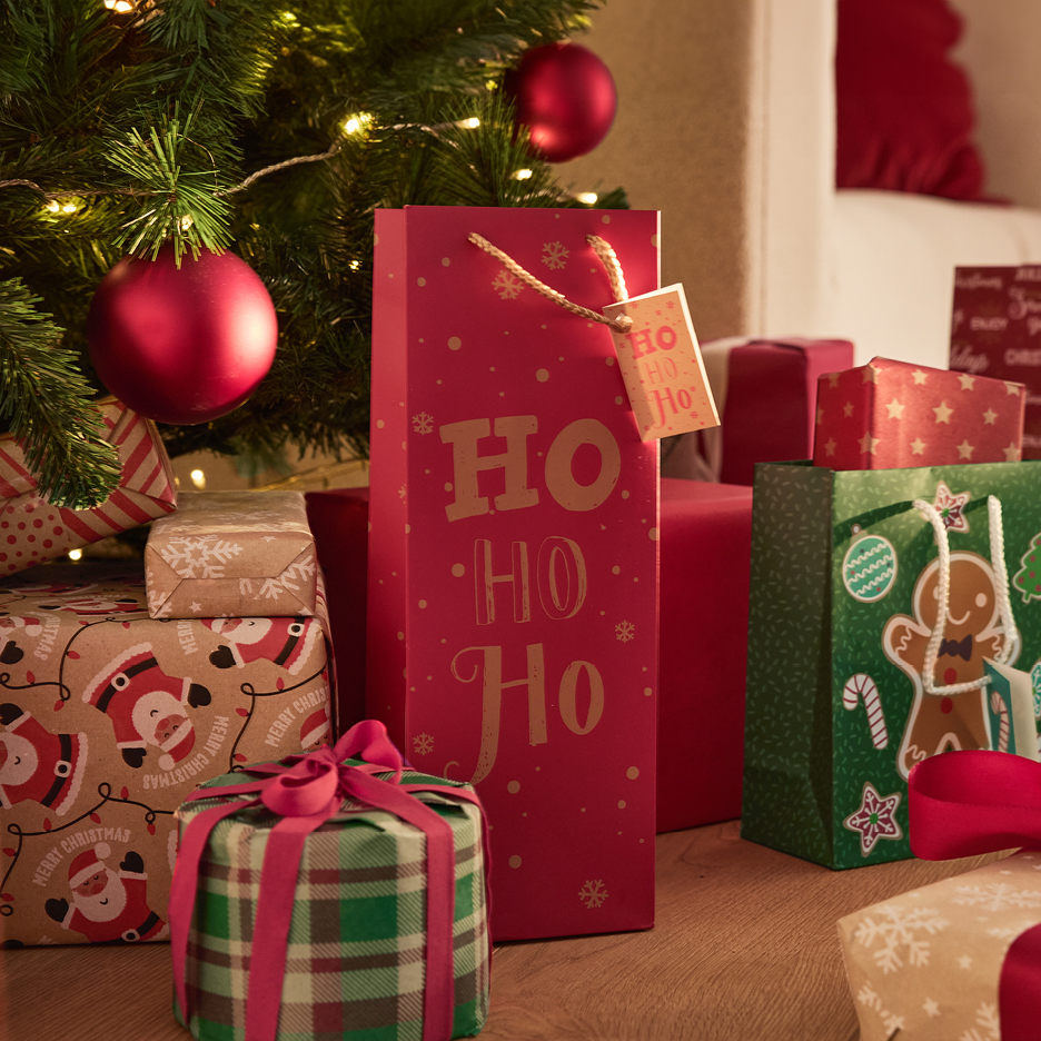 Christmas gifts and bags, including a red 'OH OH OH' bag, under a decorated Christmas tree.