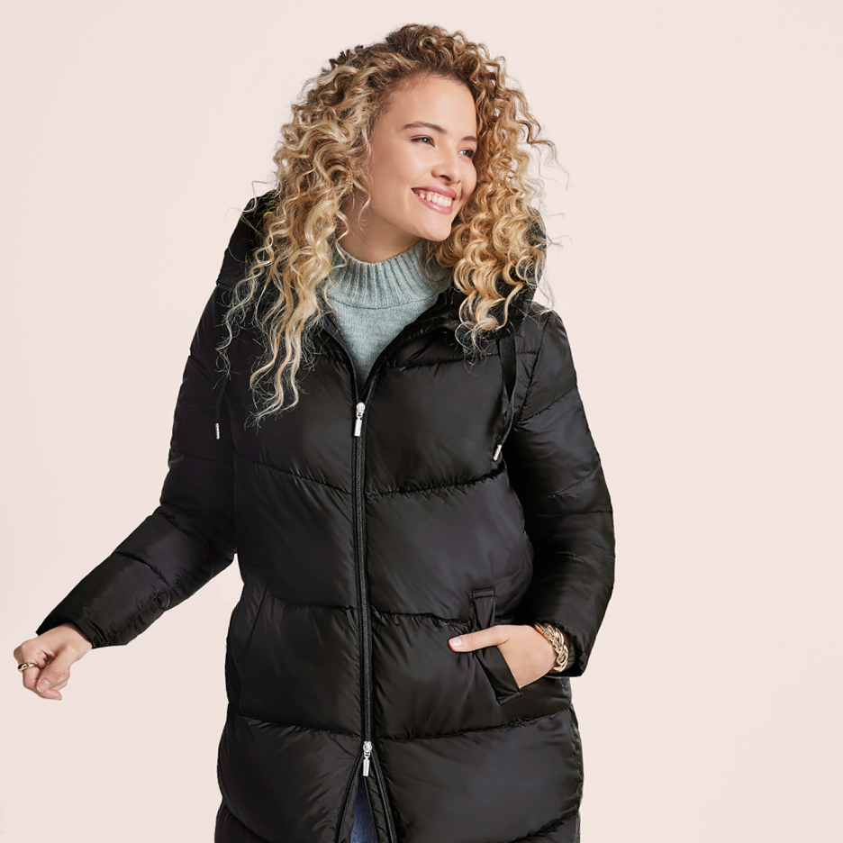 Woman in a black puffer jacket and light blue turtleneck sweater, smiling.