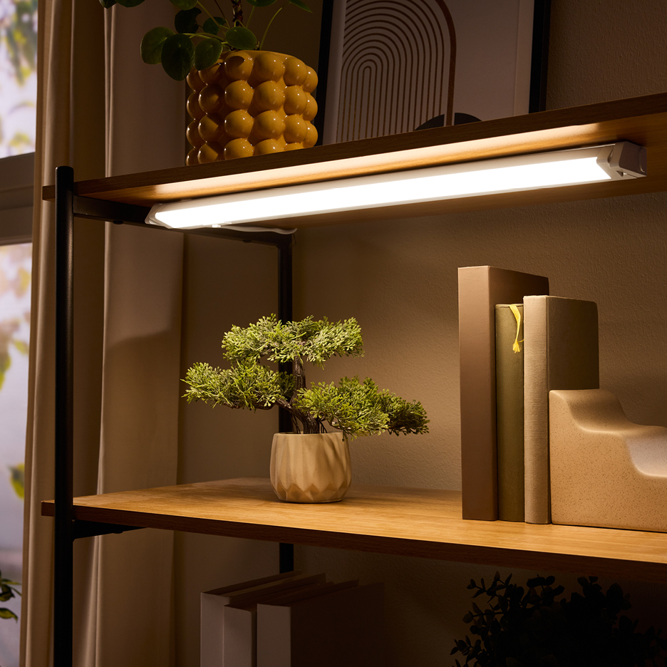 LED under-shelf light illuminating a shelf with a plant and books.