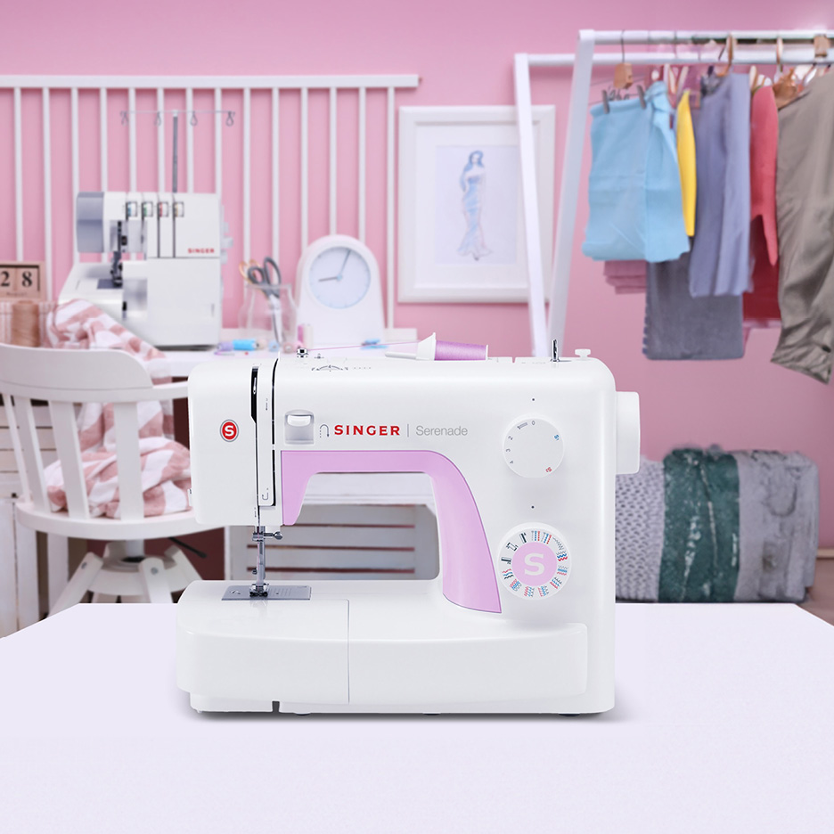 White and pink Singer Serenade sewing machine on a table in a craft room.