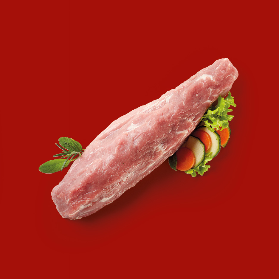 Raw pork tenderloin with herbs and sliced vegetables on a red background.